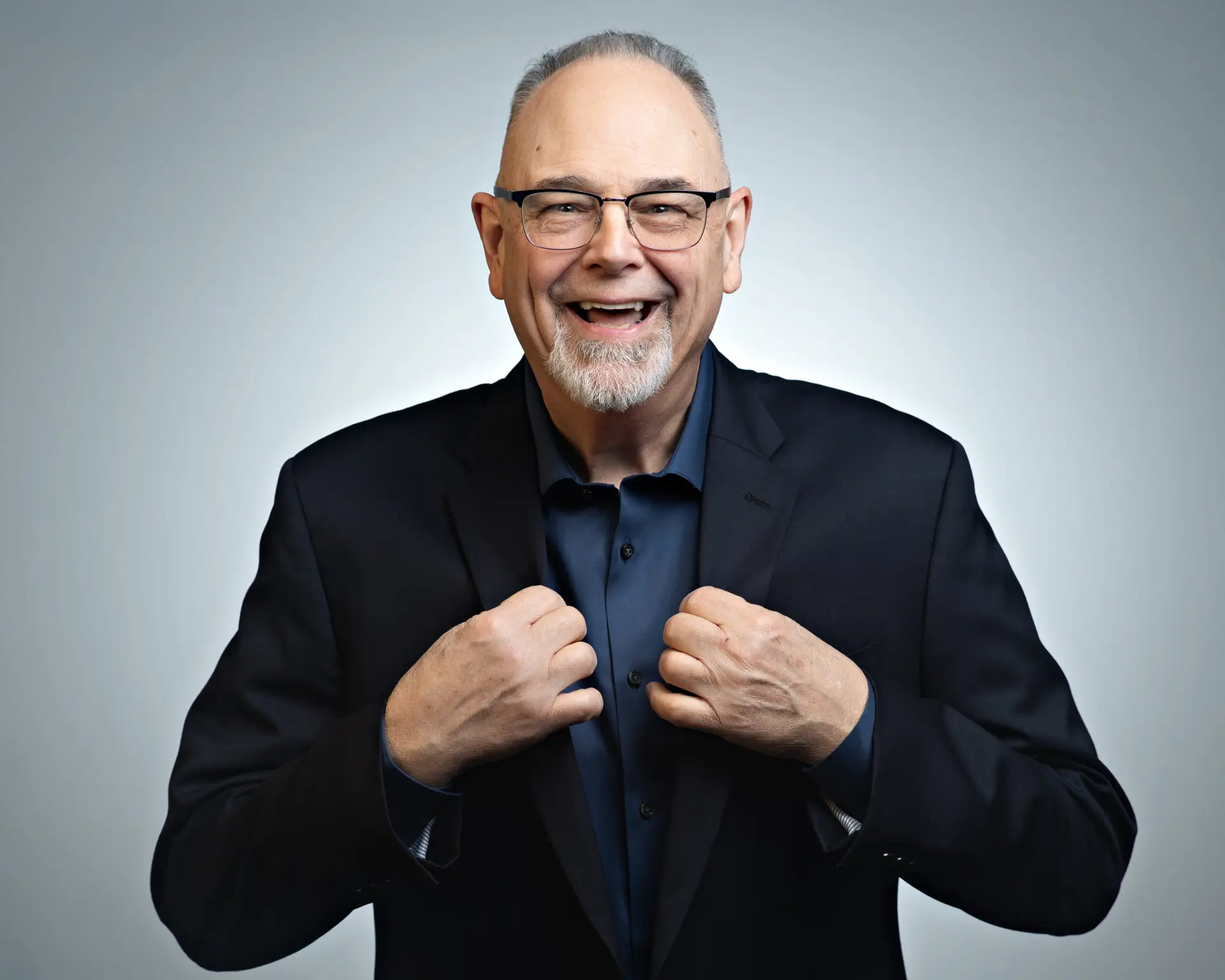 Smiling older man adjusting his suit jacket against a plain background.